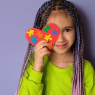 Criança de tranças segurando um cartão em formato de coração em frente ao rosto cobrindo o olho direito.